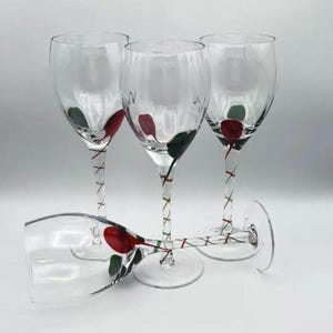 May include: Four clear glass wine glasses with long stems. Each glass features a hand-painted design of a red rose with green leaves on the bowl. The stems are decorated with a spiraling red and green striped pattern that wraps around the glass.