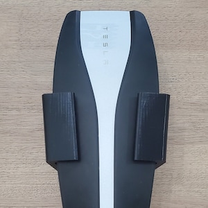 May include: A black Tesla electric vehicle charging station with a white logo and a black charging cable.