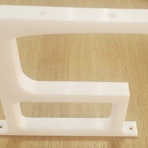 May include: White plastic shelf bracket with two holes on the top and two holes on the bottom. The bracket has a curved shape and a rectangular base.