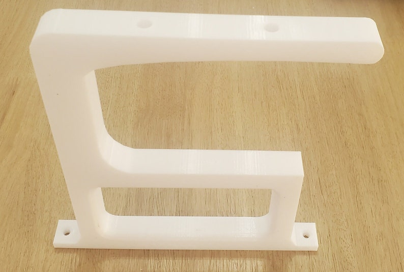 May include: White plastic shelf bracket with two holes on the top and two holes on the bottom. The bracket has a curved shape and a rectangular base.