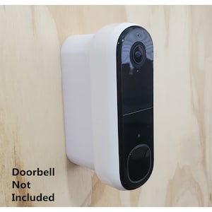 May include: A white doorbell camera with a black lens and a black button. The camera is mounted on a wooden wall. The text "Doorbell Not Included" is written below the camera.