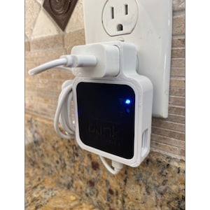 May include: A white Blink Mini security camera plugged into a standard US electrical outlet. The camera has a blue light indicating it is powered on. The camera is labeled "Blink Mini"