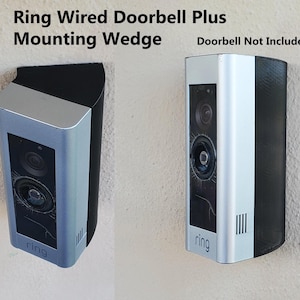 May include: A silver Ring Wired Doorbell Plus with a black mounting wedge. The doorbell is mounted on a white wall. The text "Doorbell Not Included" is visible in the image.