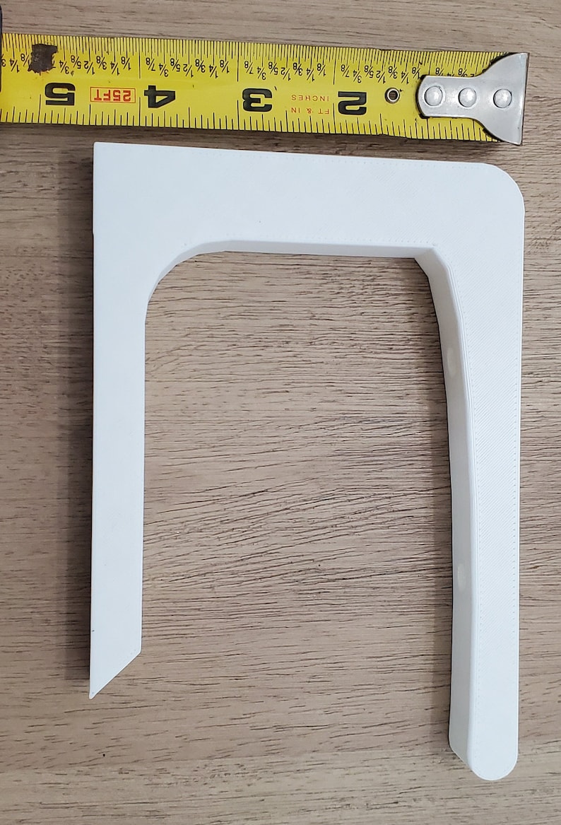 Op de afbeelding: Een witte, 3D-geprinte hoekbeugel van plastic met een afgeronde rand. De beugel is ongeveer 7,6 cm hoog en 5 cm breed.