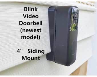 May include: Black Blink Video Doorbell (newest model) mounted on a white 4" siding mount. The doorbell has a camera lens and a button. The siding is made of horizontal panels.