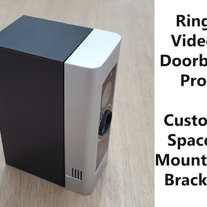 May include: A custom spacer mounting bracket for a Ring Video Doorbell Pro. The bracket is made of black and silver plastic and has a rectangular shape. It is designed to be mounted on a wall or other surface.