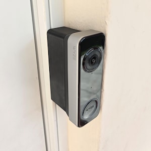 May include: A rectangular smart doorbell with a black and silver finish is mounted on a white wall. The device has a camera lens and the brand name "WYZE" is visible on the side and bottom.