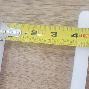 May include: A yellow measuring tape with black markings is used to measure a white object. The tape reads "25FT" and shows measurements in feet and inches.