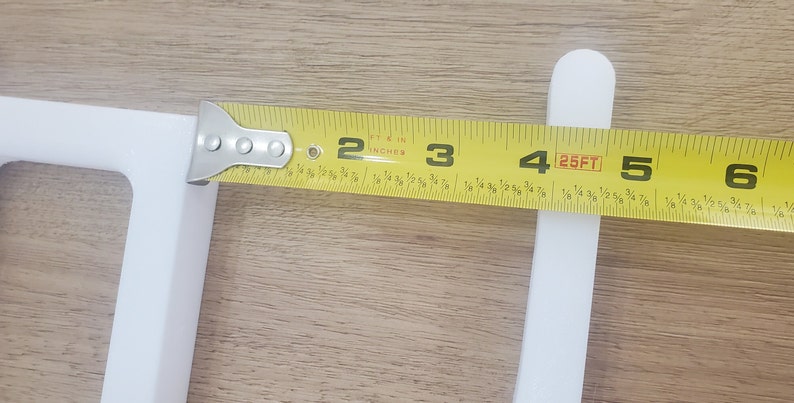 May include: A yellow measuring tape with black markings is used to measure a white object. The tape reads "25FT" and shows measurements in feet and inches.