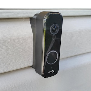 May include: A black smart doorbell with a camera lens and a large circular button. The doorbell is mounted on a white siding and has the "myQ" logo.