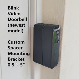 May include: A black Blink Video Doorbell (newest model) mounted on a white door frame. The image also shows a custom spacer mounting bracket, with measurements ranging from 0.5" to 5".