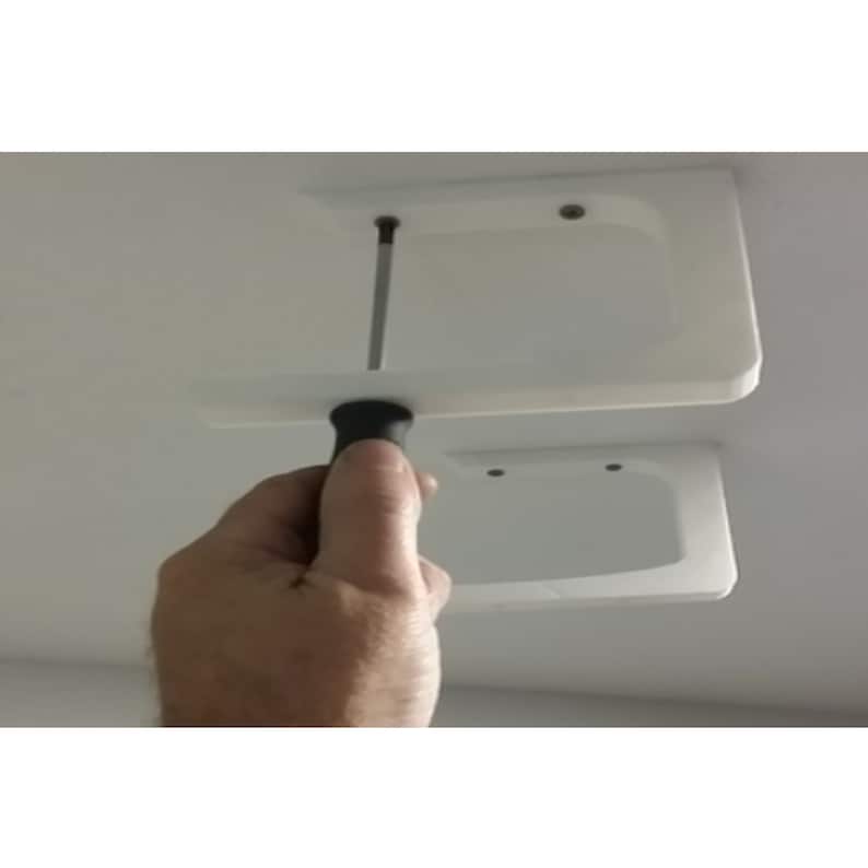 Op de afbeelding: Een witte plastic plafondbevestiging met twee schroefgaten wordt ge&iuml;nstalleerd met een zwarte schroevendraaier.