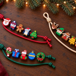 以下が含まれることがあります： クリスマスをテーマにしたカラフルなシリコンビーズ付きの装飾用ストラップ3本。赤のストラップにはサンタ、雪だるま、ジンジャーブレッドマン、ペンギン、ツリー。ベージュのストラップにはトナカイ、エルフ、家、ベル、そり。緑のストラップにはキャンディケイン、ギフト、靴下、オーナメント、リースがそれぞれ付いています。
