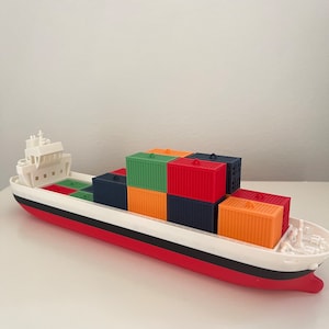 May include: A white toy cargo ship with a red bottom and black stripe, carrying a stack of colourful toy shipping containers. The containers are red, green, orange, and blue.