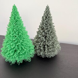 Pode incluir: Duas árvores de Natal artificiais, uma verde e outra cinza, sobre uma superfície preta.