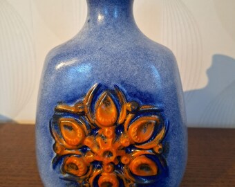 Könnte beinhalten: Eine blaue Keramikvase mit einem erhabenen orangefarbenen Blumendesign. Die Vase hat einen runden Körper und einen schmalen Hals.