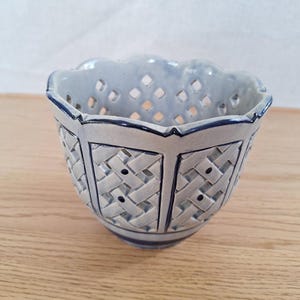 May include: A light blue ceramic basket with a woven design and scalloped rim. The basket has a geometric pattern with dark blue accents. The basket is likely used for decorative purposes.