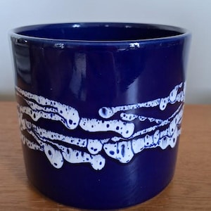 Op de afbeelding: Een blauwe keramische plantenpot met een wit abstract ontwerp. De pot heeft een gladde, glanzende afwerking.