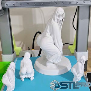 Puede incluir: Esculturas blancas impresas en 3D de una figura con una túnica con capucha y una máscara gritando. Las esculturas están en varias poses, incluyendo en cuclillas. Las esculturas están sobre una superficie azul con una impresora 3D en el fondo.