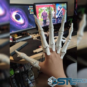 Op de afbeelding: Een witte, gelede skelet hand prop, met individuele vingersegmenten. De hand is open gehouden, met de vingers licht gebogen. De prop is ontworpen om over een echte hand te passen, waardoor een realistisch skeleteffect ontstaat. Het logo "3D STL PRO" is zichtbaar.