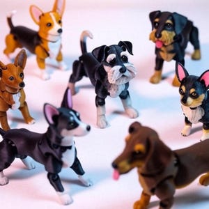 May include: A collection of articulated dog figurines in various breeds, including a dachshund, corgi, and terrier. The dogs are in different poses and feature detailed paintwork with realistic features. The figurines are set against a plain background.