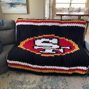 May include: A black, white, red, and gold knitted blanket with the San Francisco 49ers logo in the center.