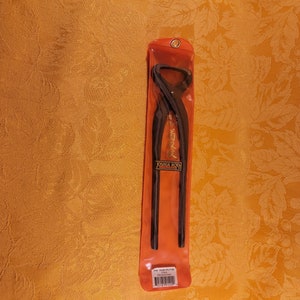 May include: Black bonsai trunk splitter tool in a clear red plastic sleeve. The tool has long, straight handles and curved blades. The text "JOSHUA ROTH" is visible on the tool. The sleeve also has text and a barcode.