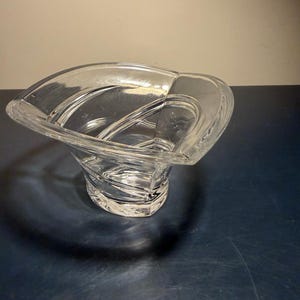 May include: A clear glass decorative bowl with a unique, curved design. The bowl has a wide, open top and a textured, spiral-like base. The bowl is made of clear glass and is suitable for decorative purposes.