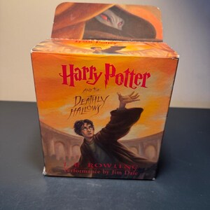 May include: A box featuring the book "Harry Potter and the Deathly Hallows" with a vibrant orange and yellow background. The title is in red, and the image shows Harry Potter with his arm outstretched. The author's name is also visible.