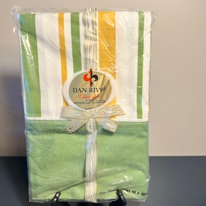 May include: A packaged set of two pillowcases, featuring a striped pattern in white, yellow, and green. The bottom portion is solid green. The packaging includes a label that reads "Dan River" and a bow.