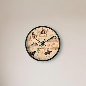 May include: A round wall clock with a black frame and a beige face featuring a repeating pattern of dark brown silhouettes of people riding horses, stylized mountain ranges, and small green and orange abstract shapes with black clock hands.