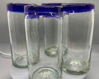 May include: Set of four clear glass tumblers with a blue rim. The glasses are stacked on a white turntable.