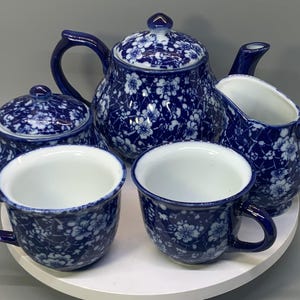 May include: A tea set featuring a teapot with a lid, a lidded sugar bowl, a creamer, and two cups. Each piece is decorated with a dark blue and white floral pattern featuring small blossoms and thin branches across the entire exterior surface.