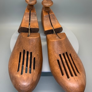 May include: Two wooden shoe trees with a brown finish and a series of holes on the sides. The shoe trees are made of wood and have a natural finish.