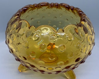 May include: A small, amber-colored glass bowl with a textured, bubbled surface. The bowl has a scalloped rim and three short legs.