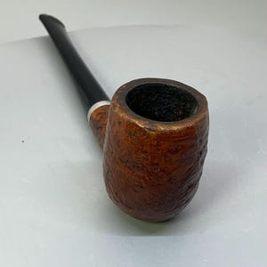 May include: A brown tobacco pipe with a textured bowl and a black stem. The pipe has a silver band near the bowl. The pipe is angled towards the upper left corner.