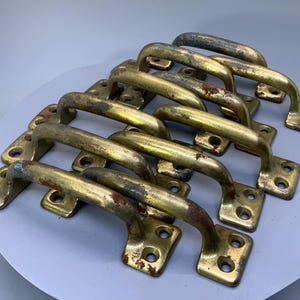 May include: A set of ten antique brass cabinet door pulls with a worn, aged finish. The pulls are all the same size and shape, with a simple, curved design.