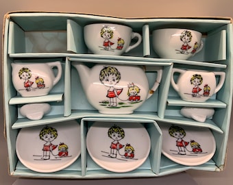May include: A vintage porcelain children's tea set in a blue box. The set includes a teapot, creamer, sugar bowl, two cups, two saucers, and two plates. Each piece features a hand-painted design of a girl pulling a toy wagon with a doll inside.