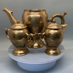 May include: A brass tea set with an ornate design. The set includes a teapot, creamer, and sugar bowl. The pieces are all decorated with intricate floral patterns.