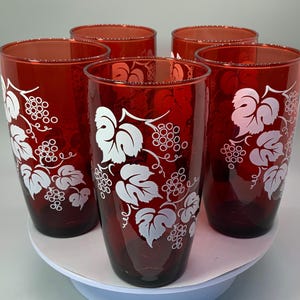 May include: Set of six red glass tumblers with white grapevine design. The glasses are clear and have a textured surface.