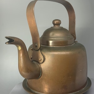 May include: A vintage copper kettle with a long spout and a handle. The kettle has a tarnished finish and a base with a raised rim.