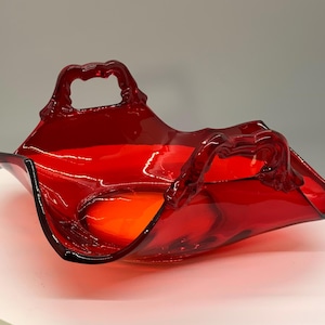May include: A vibrant red glass basket with two ornate handles. The bowl has a rectangular shape with gently curved sides. The interior of the basket has an orange hue, creating a striking contrast. This decorative piece is ideal for displaying items.