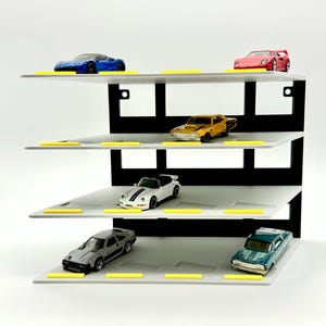 May include: A four-tier display stand featuring a black vertical back panel and light gray horizontal shelves with yellow accents. The shelves hold six die-cast toy cars in various colors including blue, red, gold, white, silver, and teal.