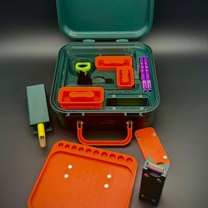 May include: A dark green carrying case with an orange handle, containing various compartments with orange and black inserts. Included are a lime green and black cylindrical container, a purple tool, and a separate orange tray with circular indentations.