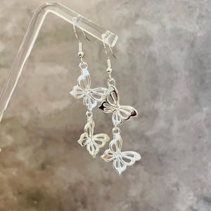 May include: Silver dangle earrings featuring three butterfly charms. Each butterfly charm has a delicate, cutout design.