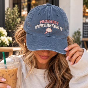 May include: A blue baseball cap with an embroidered design featuring the text PROBABLY OVERTHINKING IT in pink and white lettering, accompanied by a small white thought bubble icon with pink outlines centered on the front panel.