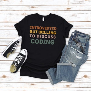 May include: Black t-shirt with the text "Introverted but willing to discuss coding" in a retro font with colourful accents.