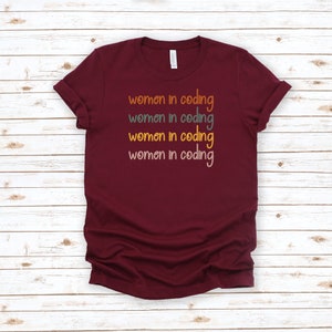 Puede incluir: Camiseta color burdeos con el texto "women in coding" repetido cuatro veces en diferentes colores.