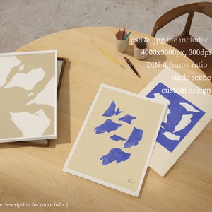 May include: Three framed abstract art prints with a beige background and blue and white shapes. The prints are on a wooden table with pencils and a chair in the background. The text on the prints reads "SL" and "custom design".