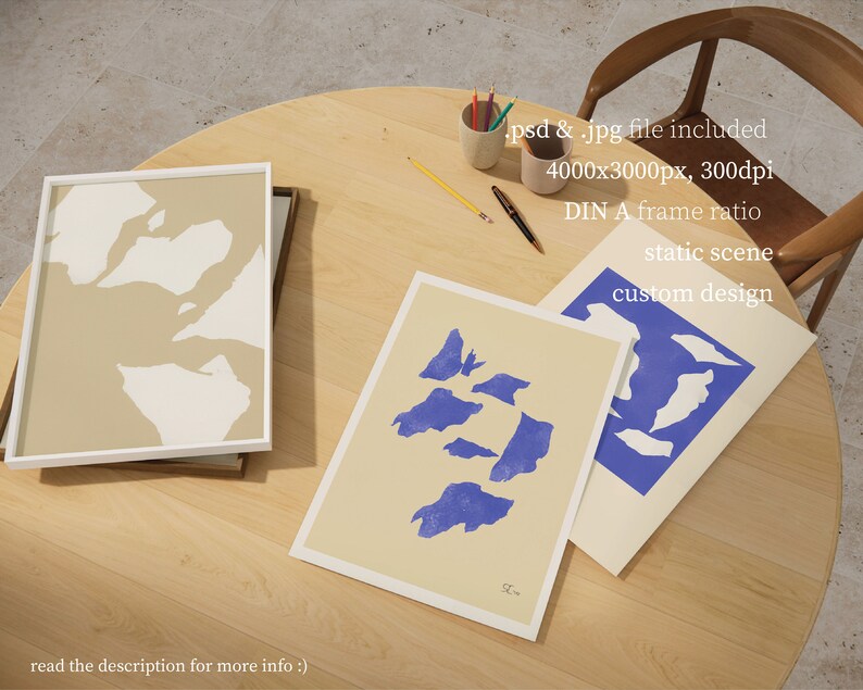 May include: Three framed abstract art prints with a beige background and blue and white shapes. The prints are on a wooden table with pencils and a chair in the background. The text on the prints reads "SL" and "custom design".